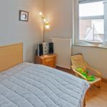 Schlafzimmer mit Bett, Nachttisch, Stuhl und Fenster. An der Wand hängt ein Bild.