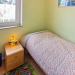Ein Schlafzimmer mit Bett, Nachttisch und Fenster. Wandfarbe ist hellgrün.
