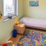 Kinderzimmer mit Bett, Schreibtisch, Spielteppich und Fenster