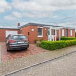 Rotes Backsteingebäude mit Garage und gepflastertem Vorplatz. Ein Auto parkt vor dem Eingang.