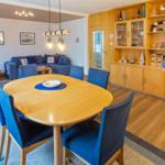 Essbereich mit runden Tisch und blauen Stühlen. Hintergrund: Wohnbereich mit Sofa und Holzmöbel.