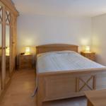 Schlafzimmer mit Holzbett, Nachttischen und Kleiderschrank. Beleuchtung durch Wandlampe und Lampen.