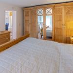 Schlafzimmer mit Holzbett, Schrank und Kommode. Durchgang zu einem weiteren Raum.