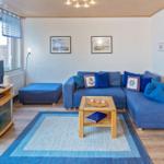 Ein Wohnzimmer mit blauem Sofa, Holzfußboden und Teppich. Fernseher und Bilder an der Wand.