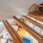 Holzgetäfelte Treppe führt zu einer Galerie mit lila Sitzgelegenheit.