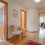 Flur mit Holztüren und Sitzgelegenheit. Blick in Küche und Wohnzimmer.