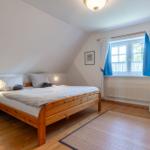 Schlafzimmer mit Holzbett, Fenster mit blauen Vorhängen und Holzboden.