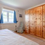 Schlafzimmer mit Holzschrank, Bett, Fenster und Stuhl.