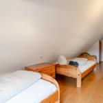 Zwei Betten mit Holzrahmen und weißer Bettwäsche in einem Dachzimmer mit Holzboden und Schiebefenster.