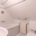 Badezimmer mit Badewanne, Waschbecken und Toilette. Weiße Fliesen mit blauer Bordüre.