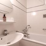 Badezimmer mit Badewanne, Waschbecken und runden Spiegel. Weiße Fliesen mit blauen Akzenten.