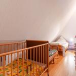 Kinderzimmer mit Babybett, Bett und Schrank unter Dachschräge.