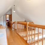 Dachgeschoss mit Holzbett, Treppenhaus und Sessel. Holzfußboden und weiße Wände.
