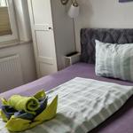 Schlafzimmer mit Bett, Kissen und Handtüchern. Fenster, Schrank und Wandlampe sichtbar.