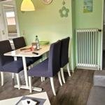 Esszimmer mit Tisch, vier Stühlen und grünen Wänden. Sofa und Heizung sind sichtbar.
