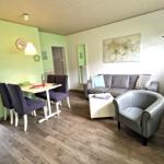 Wohn- und Essbereich mit Sofa, Sessel, Tisch und Stühlen. Wandbild und Holzboden.