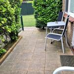 Terrasse mit Tisch, zwei Stühlen und grünen Hecken. Hinterhof mit Zaun und Rasen.