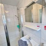 Badezimmer mit Dusche, Waschbecken und Spiegel.