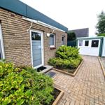 Haus mit braunem Steinmauerwerk, weiße Tür mit Nummer 4 und gepflasterter Außenbereich mit Beeten.