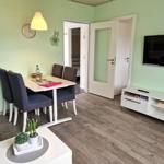 Wohnzimmer mit Esstisch, Fernseher und Tür zum Schlafzimmer.