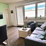 Wohnzimmer mit Sofa, Sessel, Couchtisch und Fernseher an der Wand.