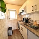 Küche mit Spüle, Herd, Kühlschrank und Mikrowelle. Wandfliesen und Holzboden.