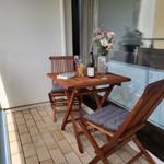 Terrasse mit Holztisch, zwei Stühlen, Blumen und Weinflasche.