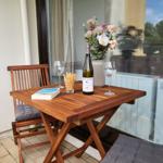 Holztisch mit Stuhl, Weinflasche, Gläsern und Blumen auf Balkon.