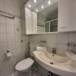 Badezimmer mit Waschbecken, Spiegel, Toilette und Handtuchhaltern.