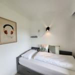 Schlafzimmer mit Bett, Wandbildern und Wandlampe.