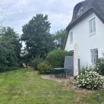 Haus mit strohgedecktem Dach und Garten mit Tisch, Stühlen und Blumen.