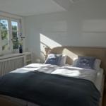 Schlafzimmer mit Doppelbett, Fenstern und Nachttisch.