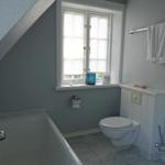 Badezimmer mit Badewanne, Toilette und Fenster mit Jalousie.
