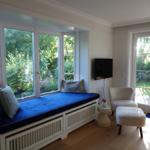 Raum mit Sitzbank vor Fenster, Sessel und Fernseher.