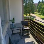 Balkon mit Tisch, zwei Stühlen und Pflanze. Blick auf Grünfläche und Bäume.