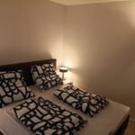 Schlafzimmer mit Bett, Kissen und Decke mit schwarz-weißem Muster, Nachttisch und Wand-TV.
