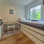 Zimmer mit zwei Betten, Schreibtisch und Fenster mit Blick auf Grün.