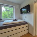 Schlafzimmer mit Bett, TV und Fenster mit Blick auf Bäume.