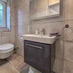 Badezimmer mit Toilette, Waschbecken und Spiegelschrank. Fenster und Handtuchhalter sichtbar.