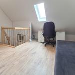 Dachgeschosszimmer mit Schreibtisch, Drehstuhl und Schlafcouch unter Dachschrägen.