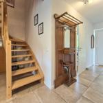 Hausgang mit Holztreppe, Garderobenmöbel und Fliesenboden.