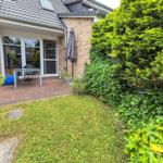 Hinterhof mit Terrasse, Sitzgelegenheit und grüner Hecke.
