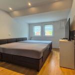 Schlafzimmer mit Doppelbett, zwei Fenstern und TV-Schrank.