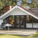Terrasse mit Tisch und Stühlen vor einem Haus mit Glasfront und Schornstein.
