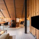 Wohnraum mit Holzwand, Kamin und TV. Essbereich mit Tisch und Stühlen.