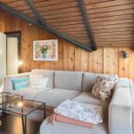 Wohnzimmer mit Sofa, Couchtisch und Holzwand. Deckenbalken und Fenster sichtbar.