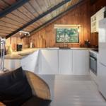 Küche mit weißen Schränken, Kühlschrank und Arbeitsfläche unter Holzdecke.