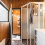 Badezimmer mit Dusche, Waschbecken und Holzwandverkleidung.