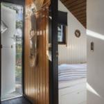 Schlafzimmer mit Bett und Holzwand. Tür führt nach draußen.