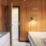 Schlafzimmer mit Holzwand, Bett, Nachttisch und Tür zum Bad.